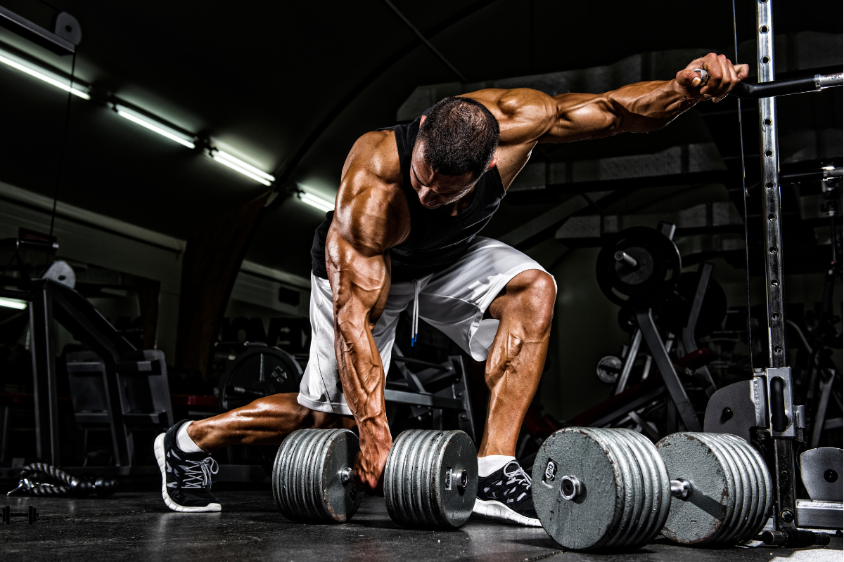 A man doing single arm bent over rows with two large dumbbells on the ground. His veins on his legs pop out, as if he's had a great workout.