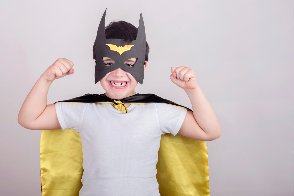 A child wearing a batman mask and cape, he is flexing.