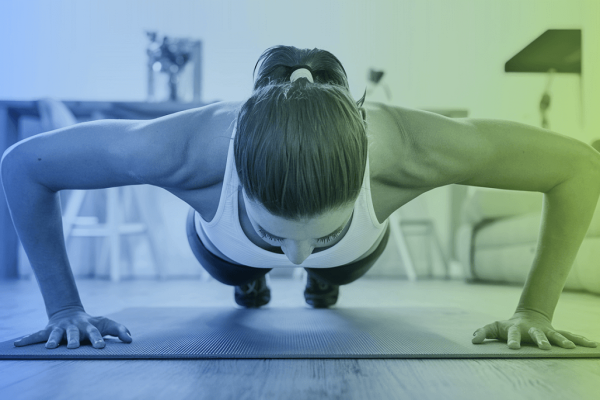 A woman is doing pushups on a yoga mat, presumably in her home or living room. She isn't using weights to workout her arms or chest.