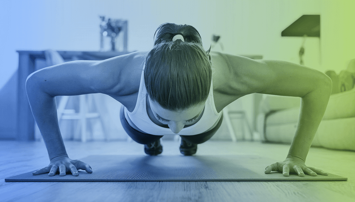 A woman is doing pushups on a yoga mat, presumably in her home or living room. She isn't using weights to workout her arms or chest.